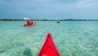 View from a person sitting in a sea kayak as another red sea kayak paddles perpendicular to them in Cuba on a sunny day